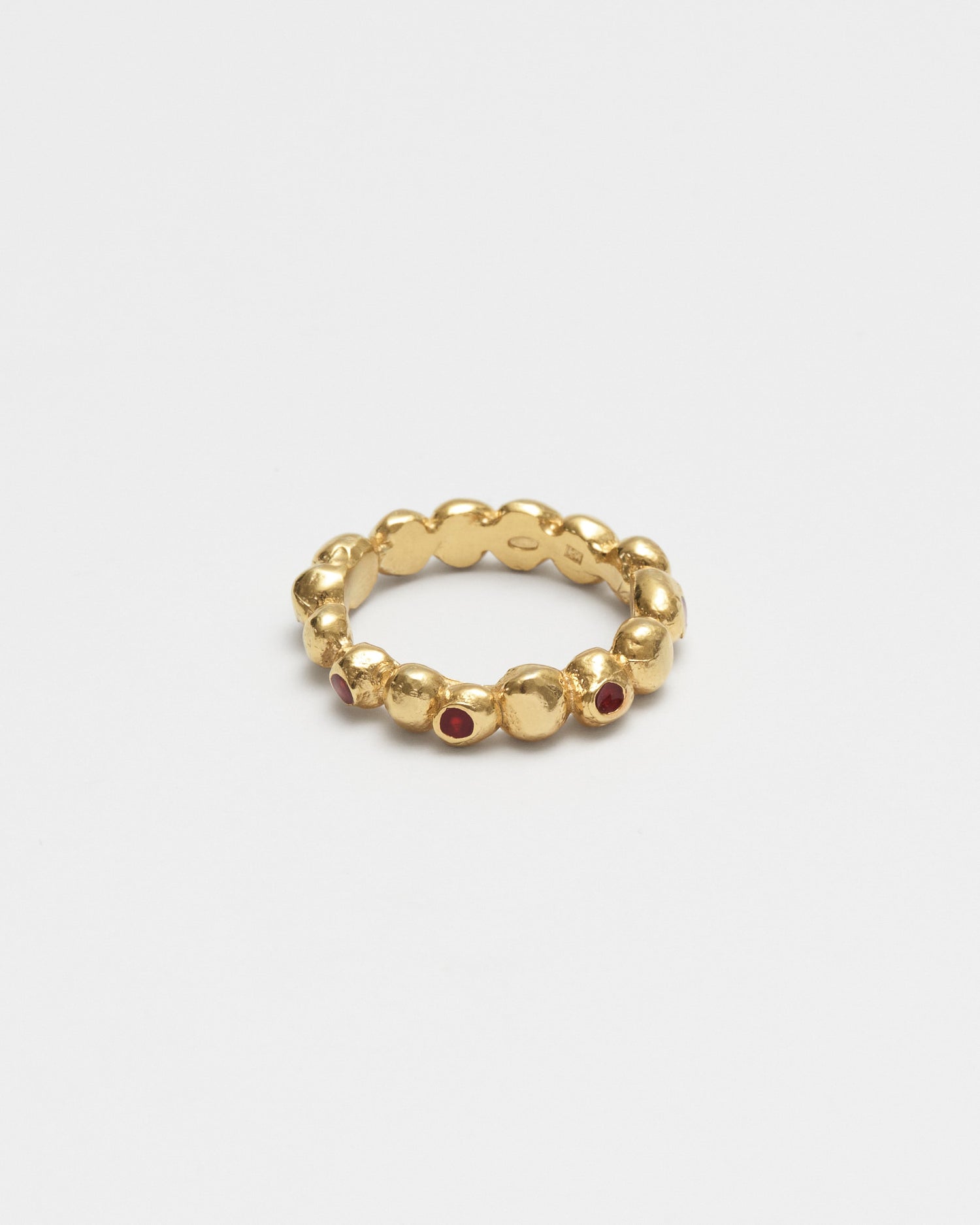 A gold beaded stretch ring with small red gemstone accents, photographed on a clean light gray background.