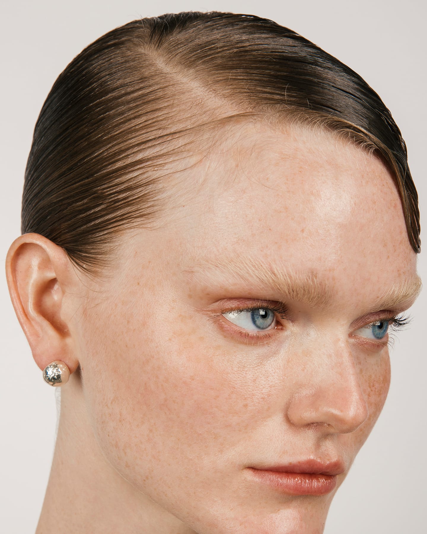 Close-up of a person with slicked-back hair and blue eyes on a plain background wearing the LMJ Meteora Earrings in Silver