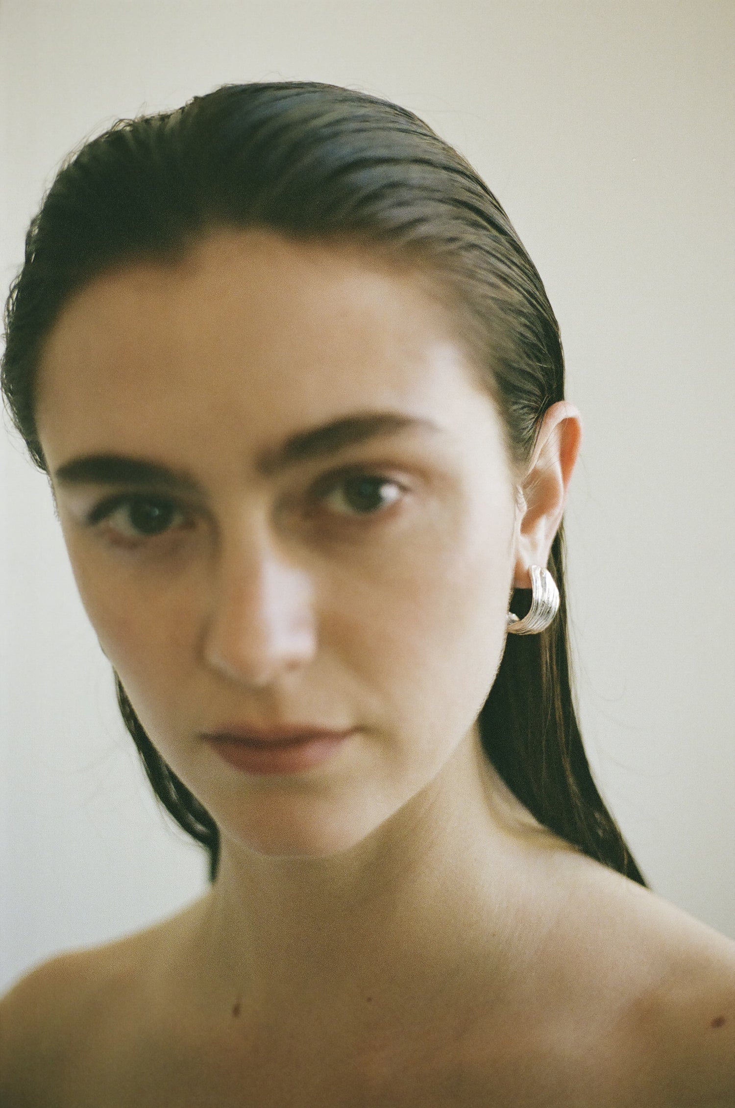 Close-up of a person with wet hair and silver Twist Earrings against a plain background