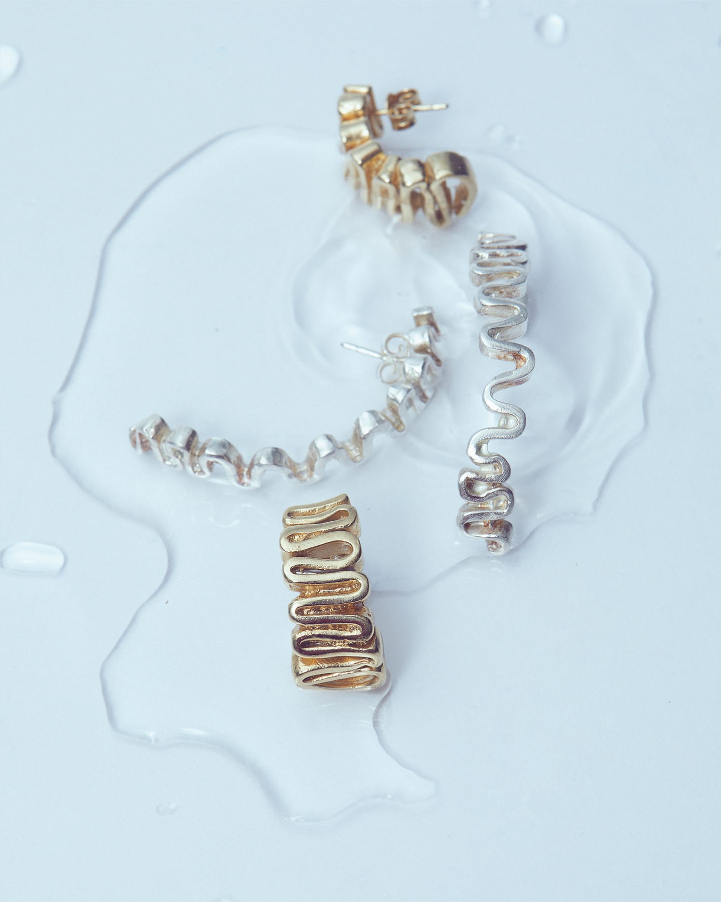 Gold and silver Arpa earrings styled on a wet glass surface