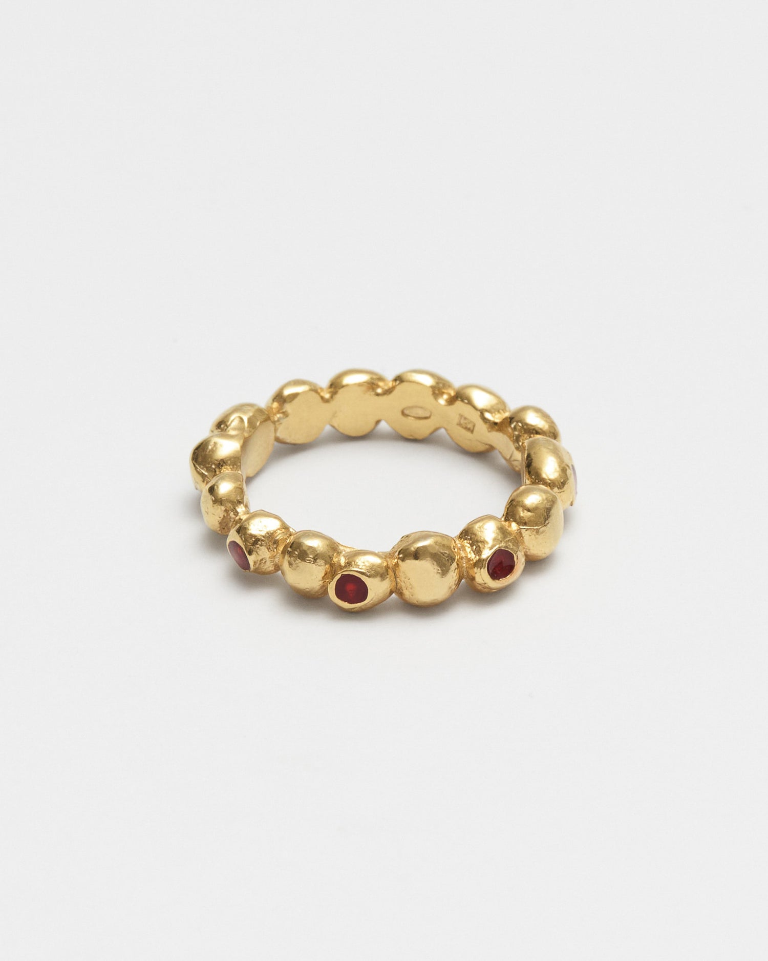 A gold beaded stretch ring with small red gemstone accents, photographed on a clean light gray background.