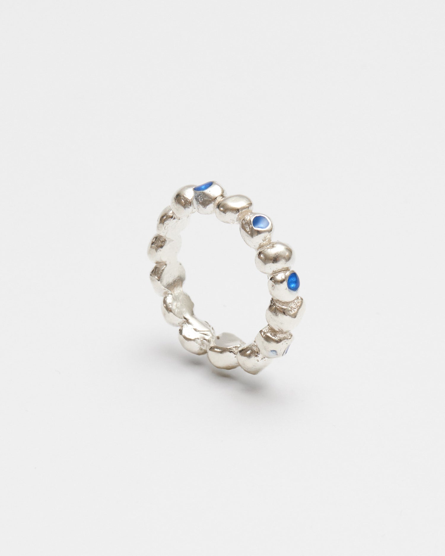 A textured sterling silver band ring featuring small, irregularly shaped silver beads and tiny blue stone accents, shown on a clean light gray background.