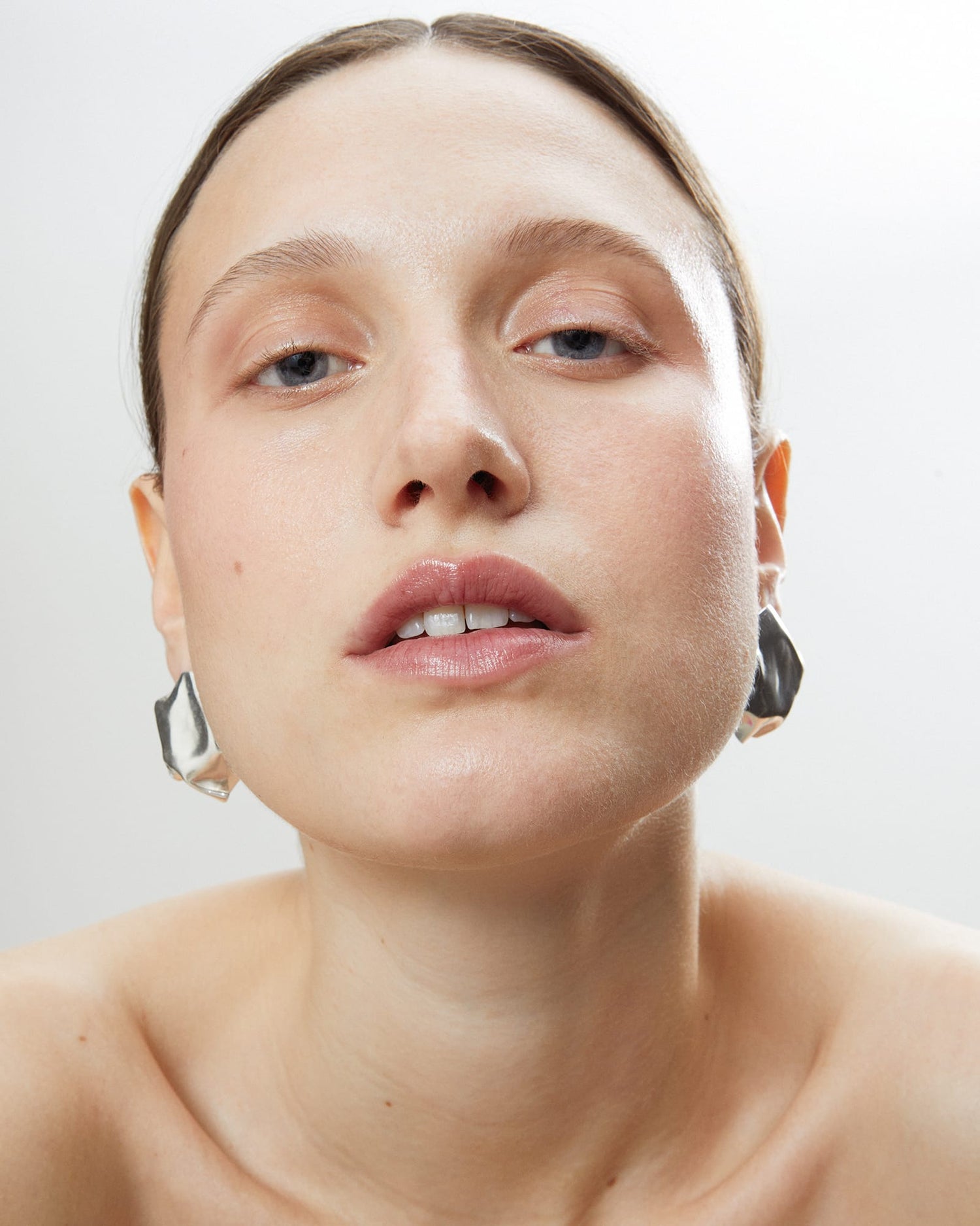 Close-up of a model wearing LMJ Blow Earrings in silver, styled with natural makeup and slicked-back hair.