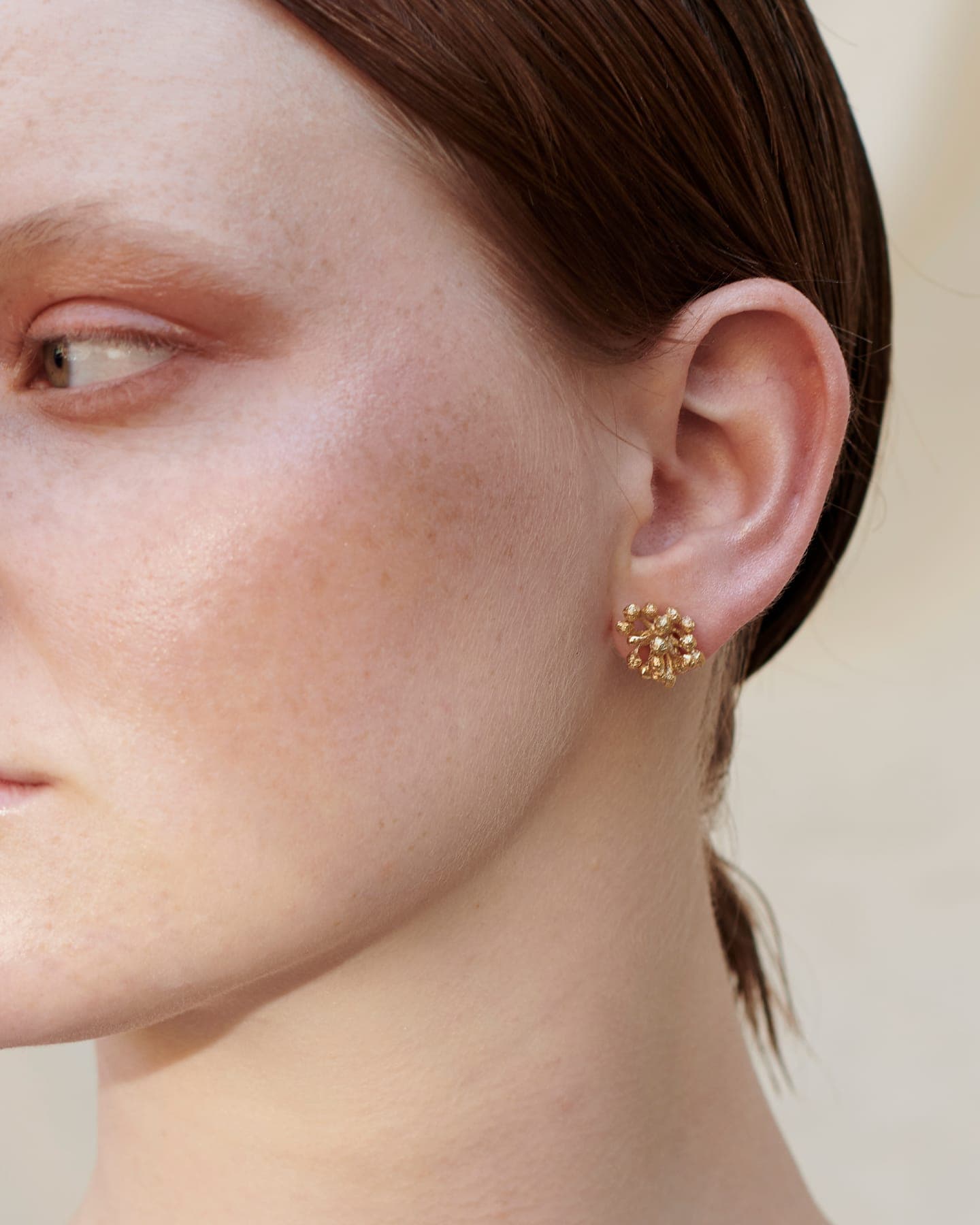 Close-up of a person wearing gold floral  LMJ Bouquet Maxi earrings on a neutral background