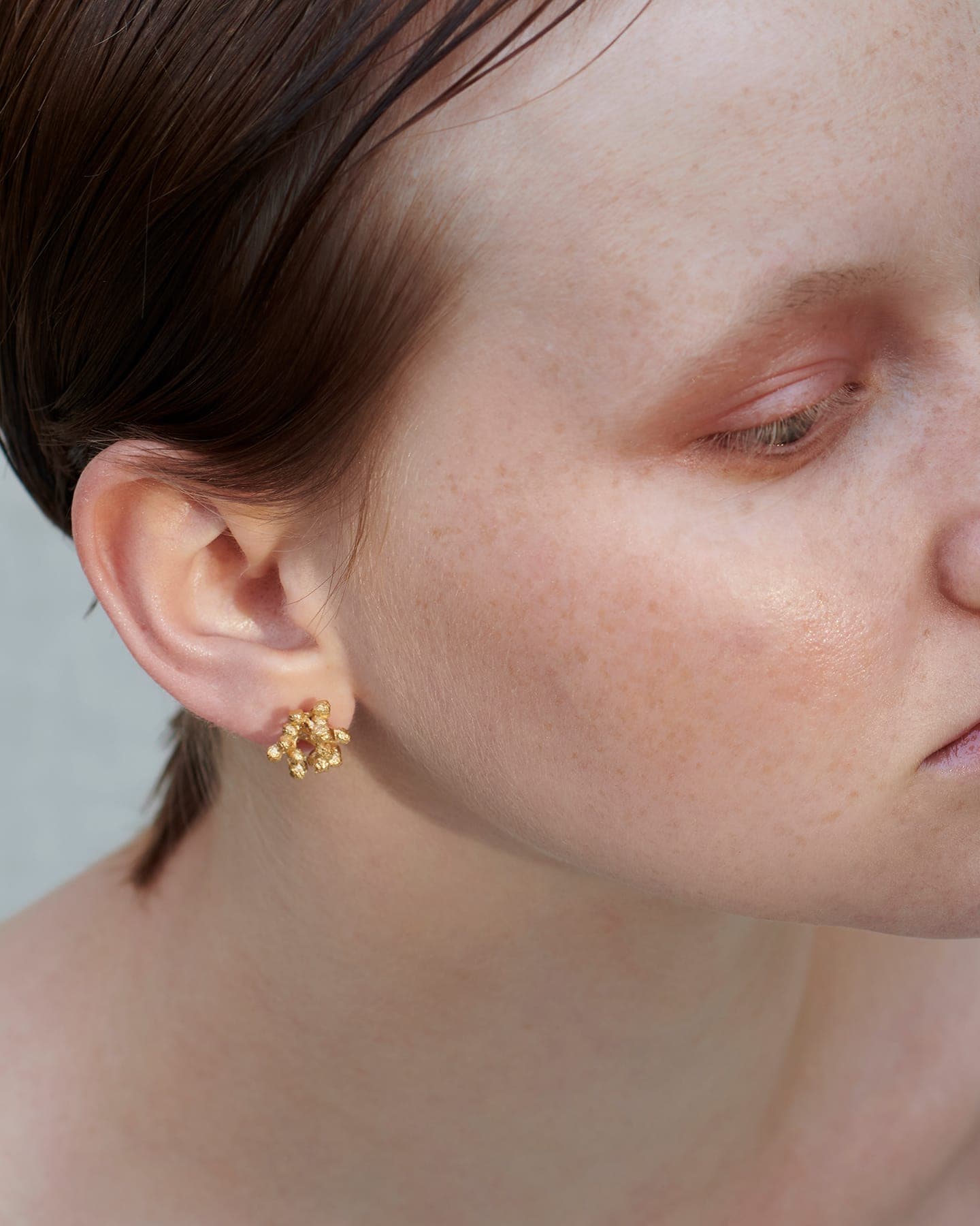 LMJ Close-up of a person wearing gold earrings with a neutral background