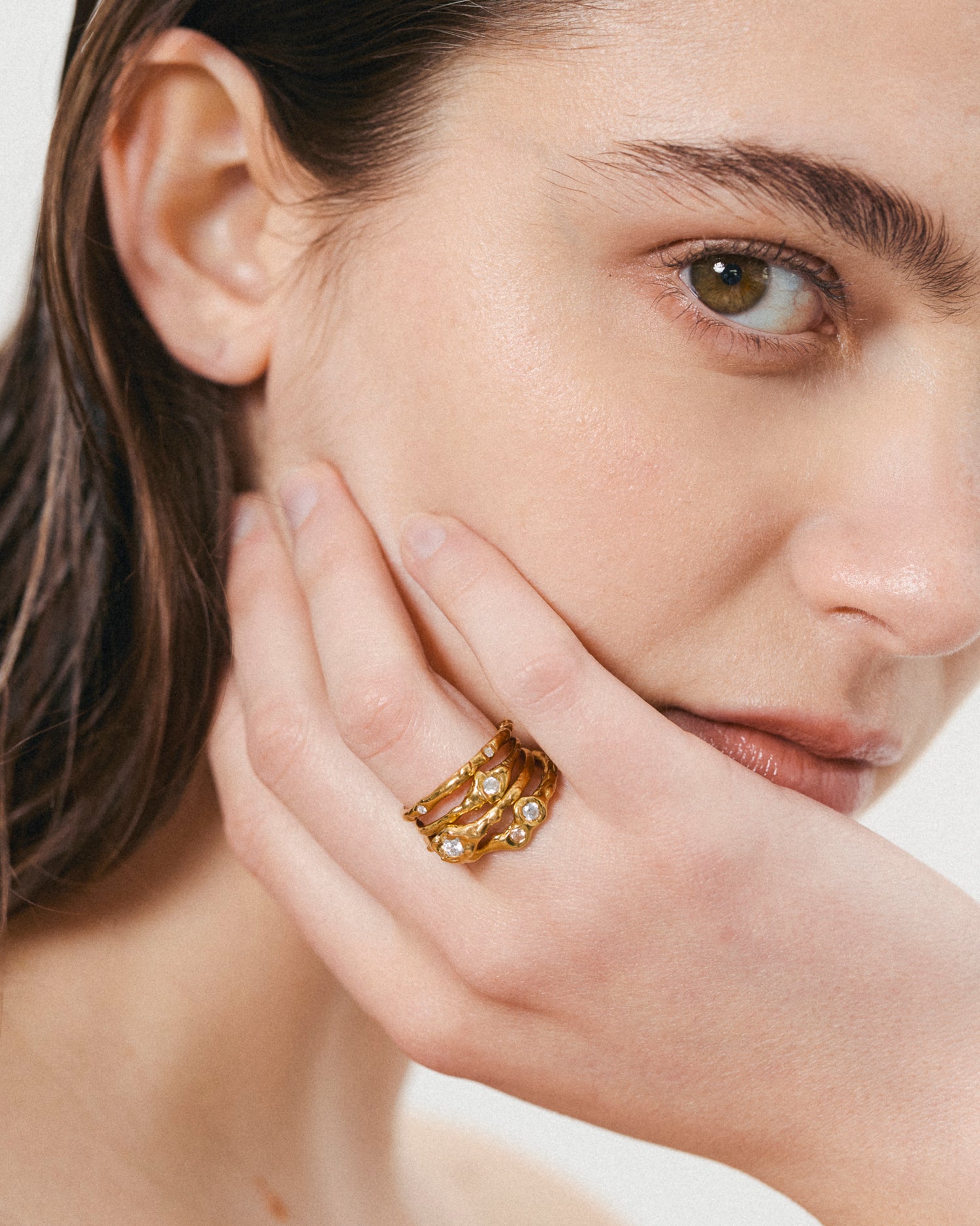 Close-up of a woman wearing a gold ring on her finger against a neutral background