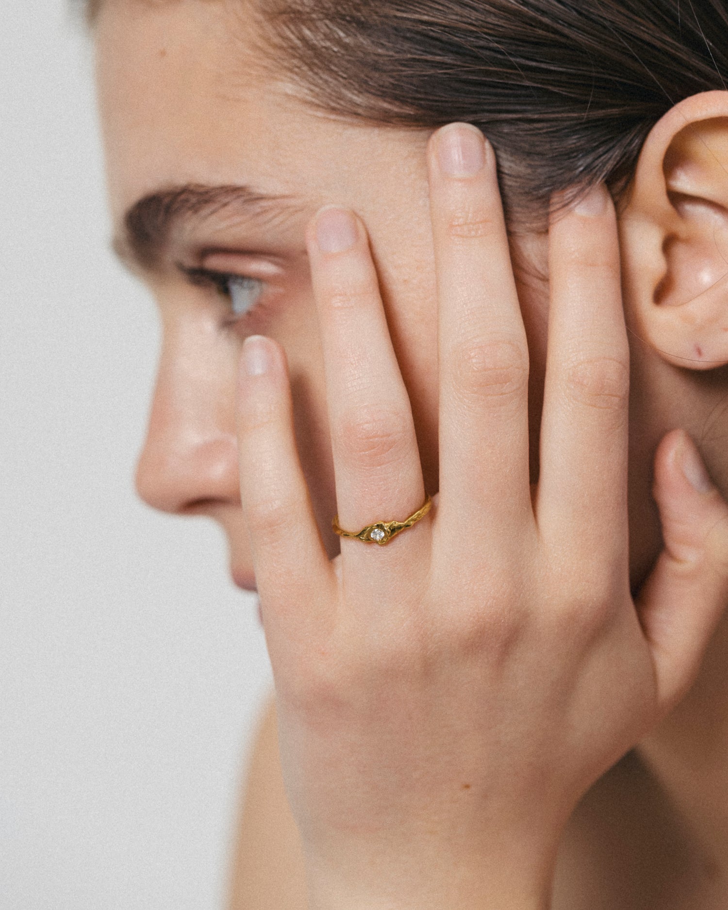 Close-up of a person wearing a gold ring on their finger, with a neutral background.