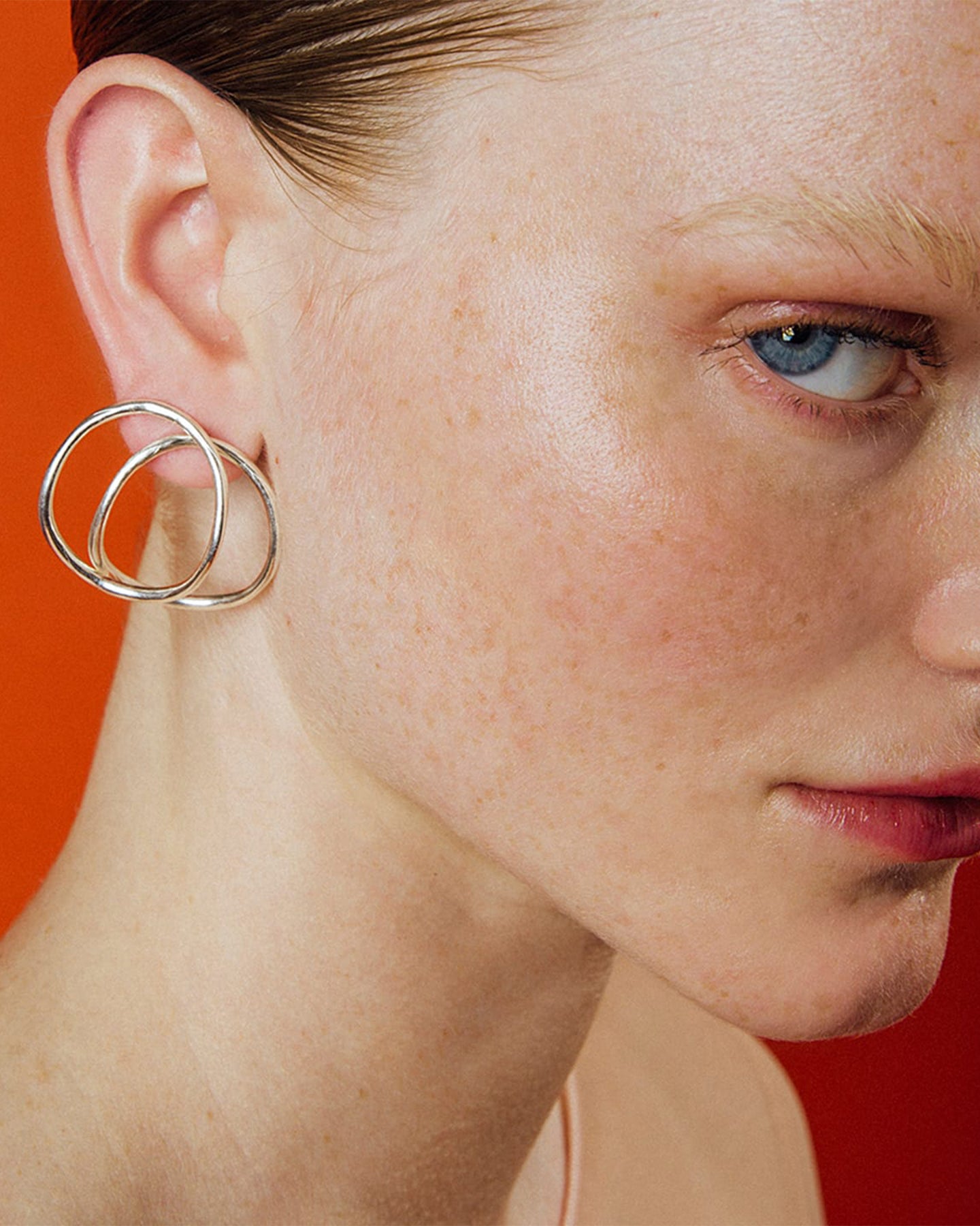 Close-up of a person wearing the hollow silver hoop earring against an orange background. 