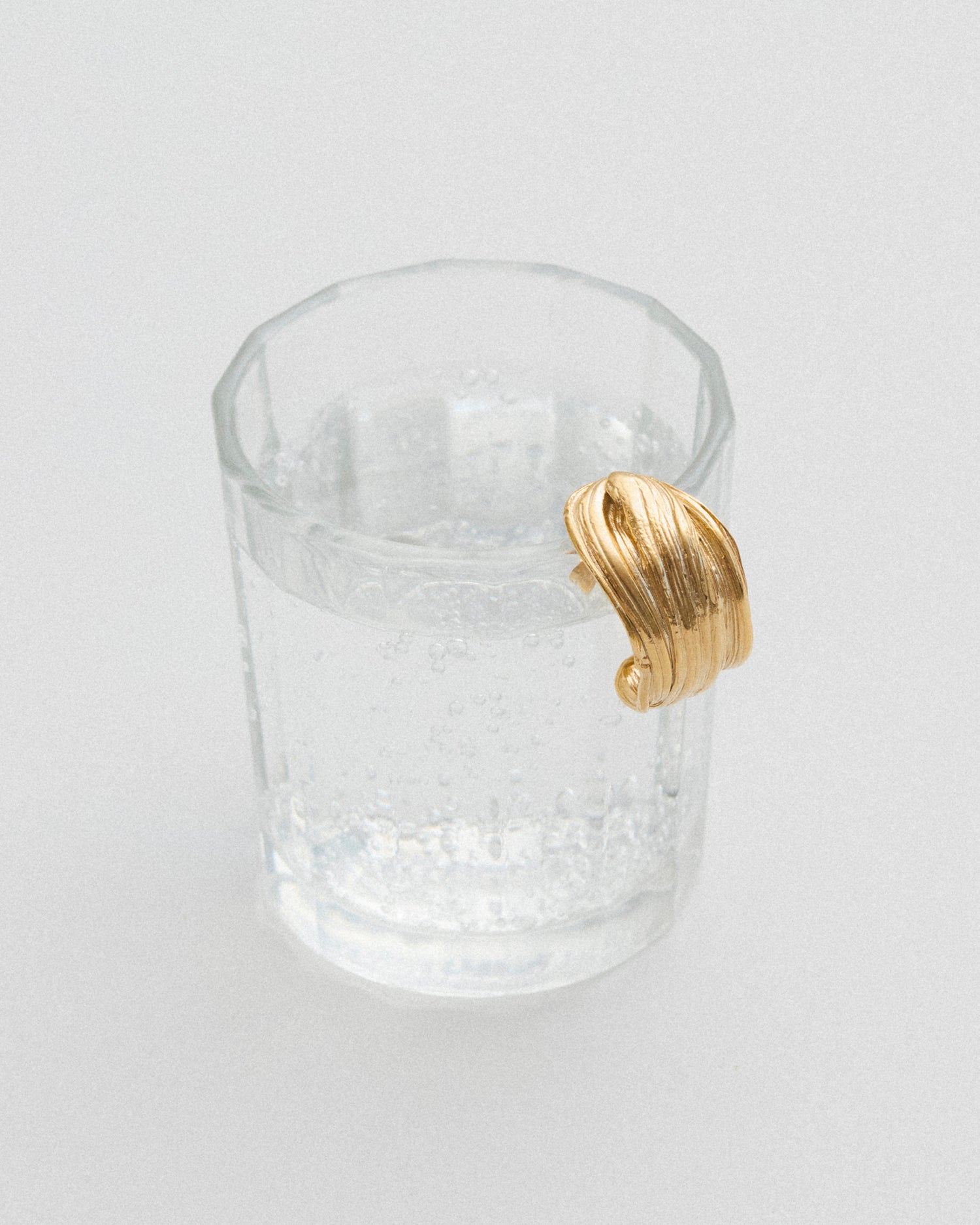 LMJ Twist Earring in gold resting on a glass – fluid design and golden shimmer