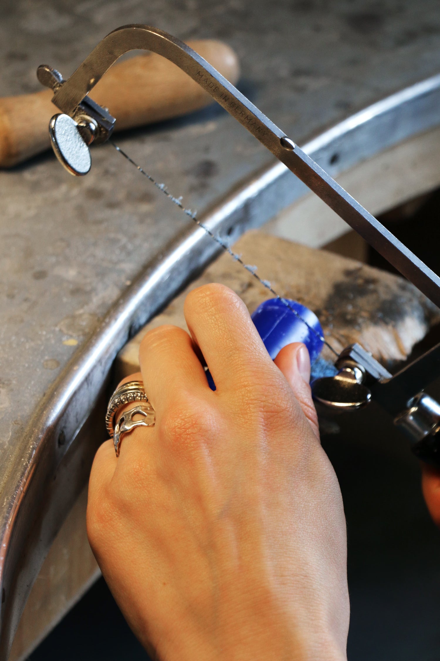 Hand using a hacksaw to cut metal on a workbench.